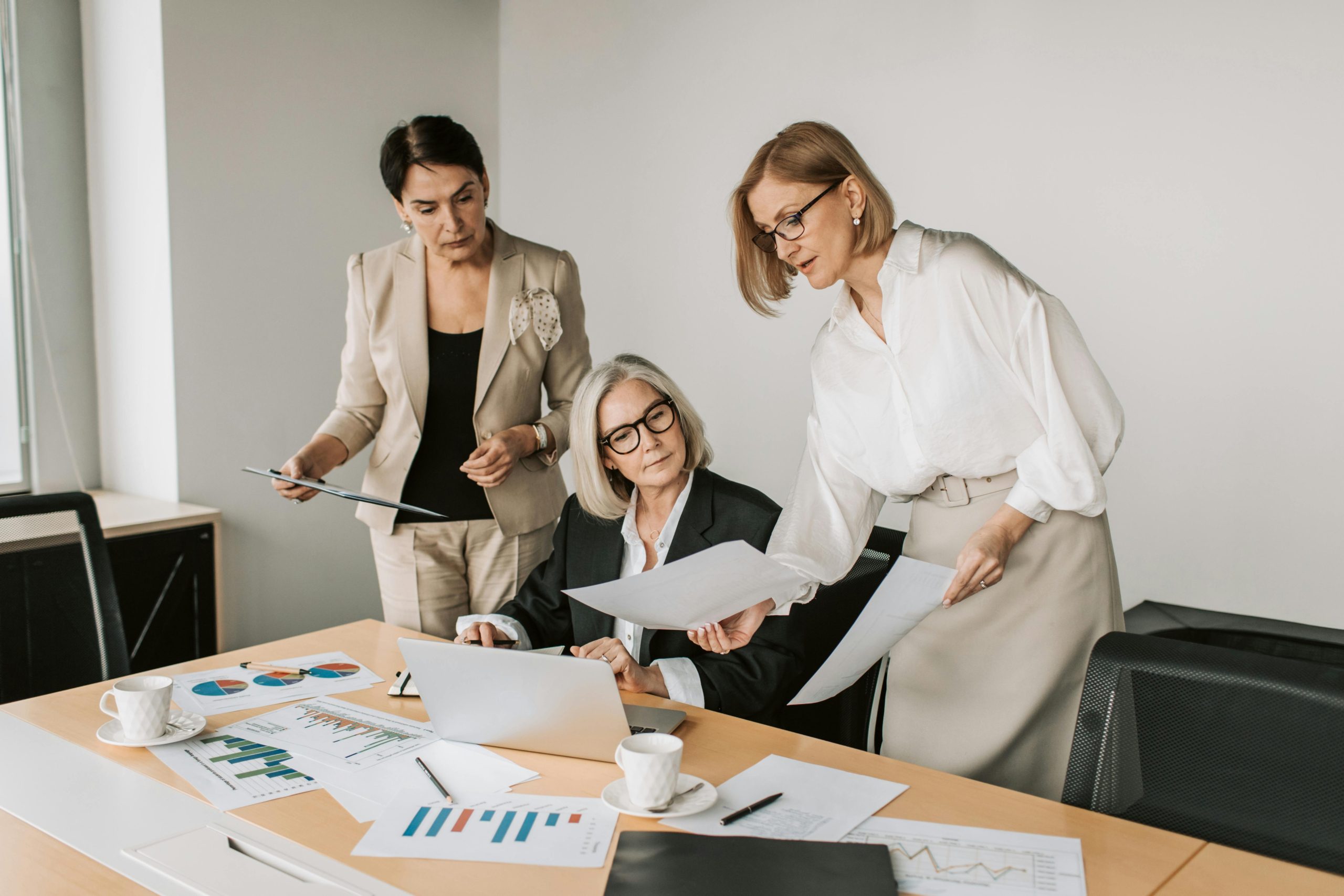 Three businesswomen discussing reports in a modern office environment.