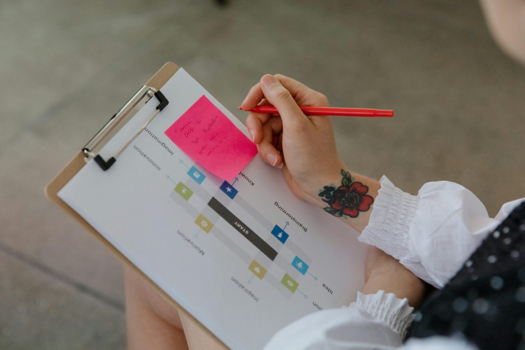 Close-up of a person using a red pen on a sticky note attached to a chart on a clipboard.